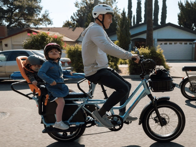 A parent rides a cargo ebike with a child on the rear seat