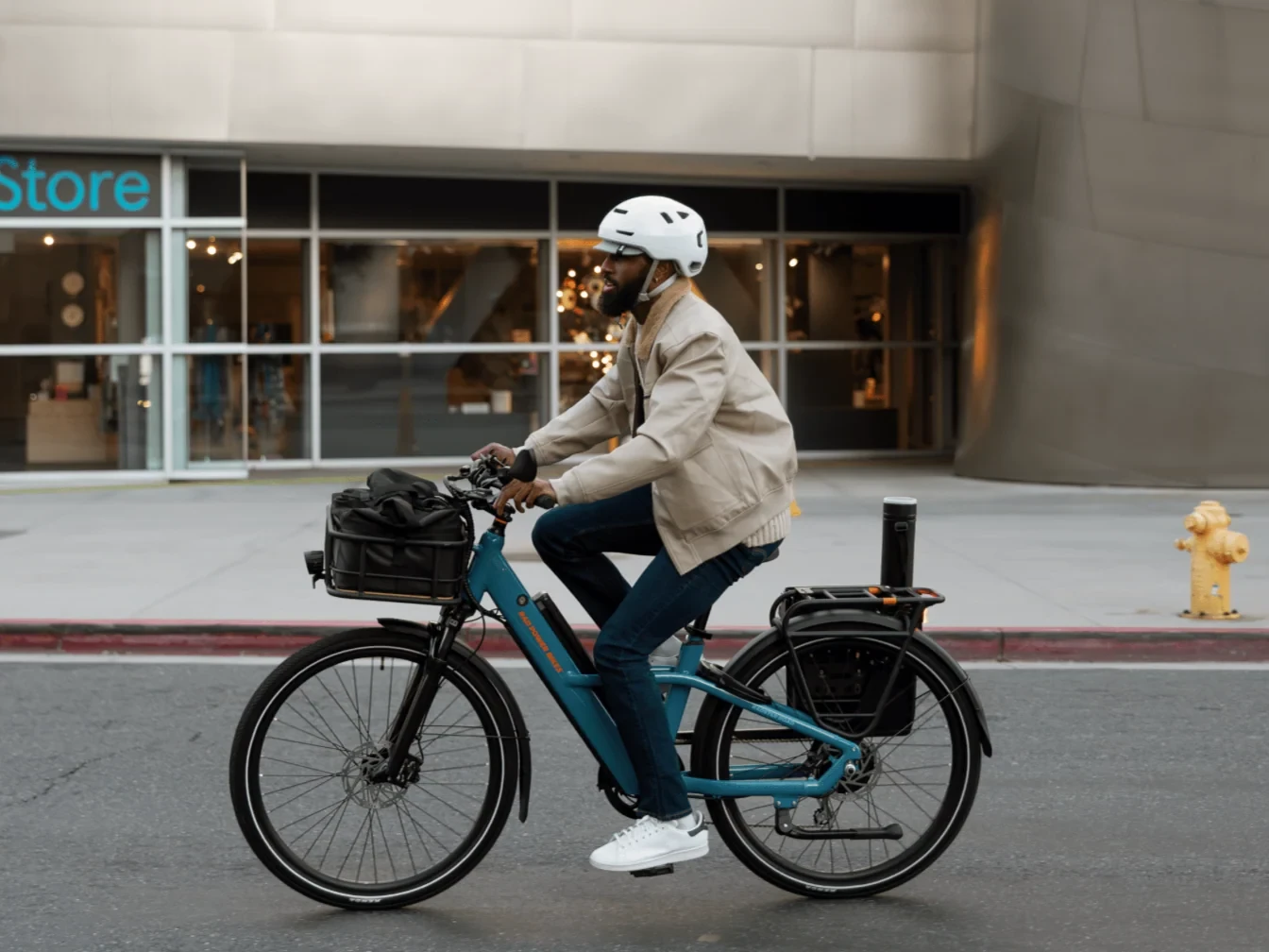 A rider in a white helmet cruises past a storefront on a teal step-thru ebike