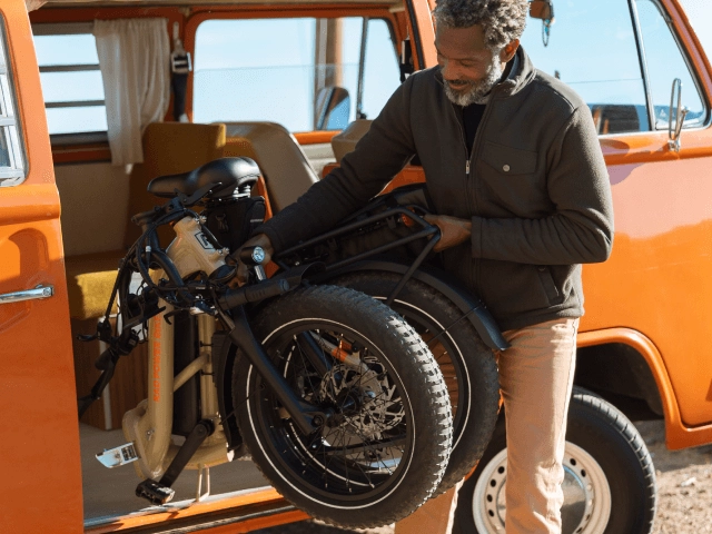 A man folds a Rad ebike into the back of an orange camper van
