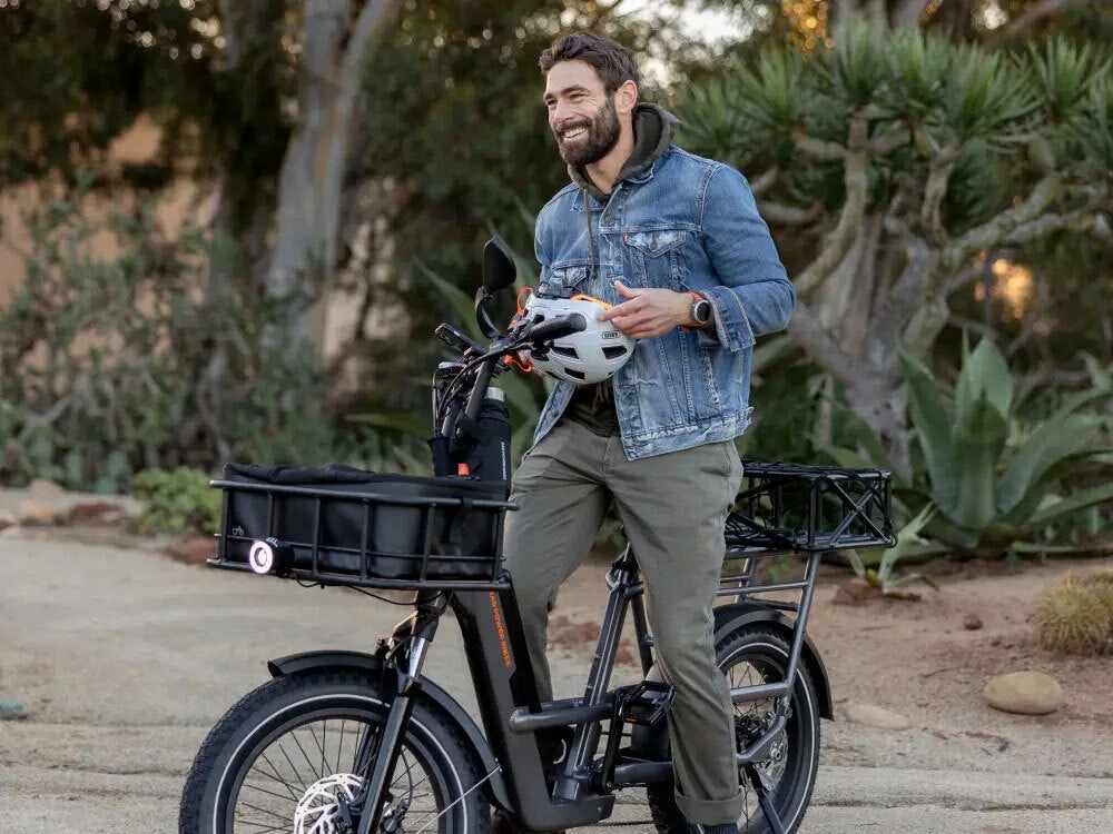 A man in a denim jacket and helmet stands with a black Rad ebike with a front basket