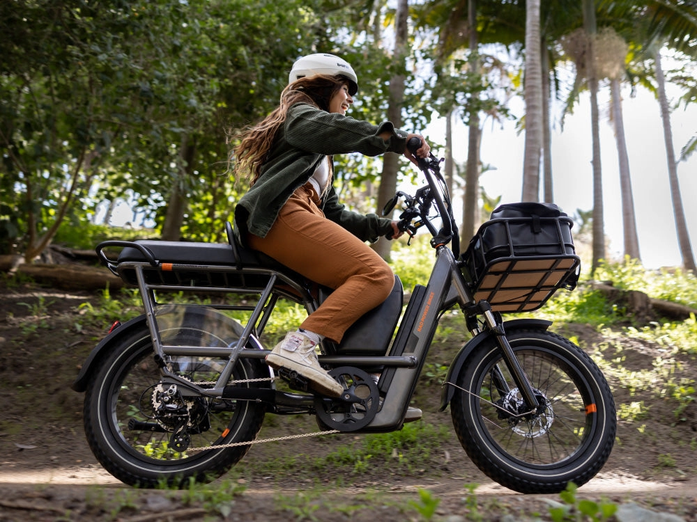 A rider with a basket on a black cargo ebike on a sunny park path