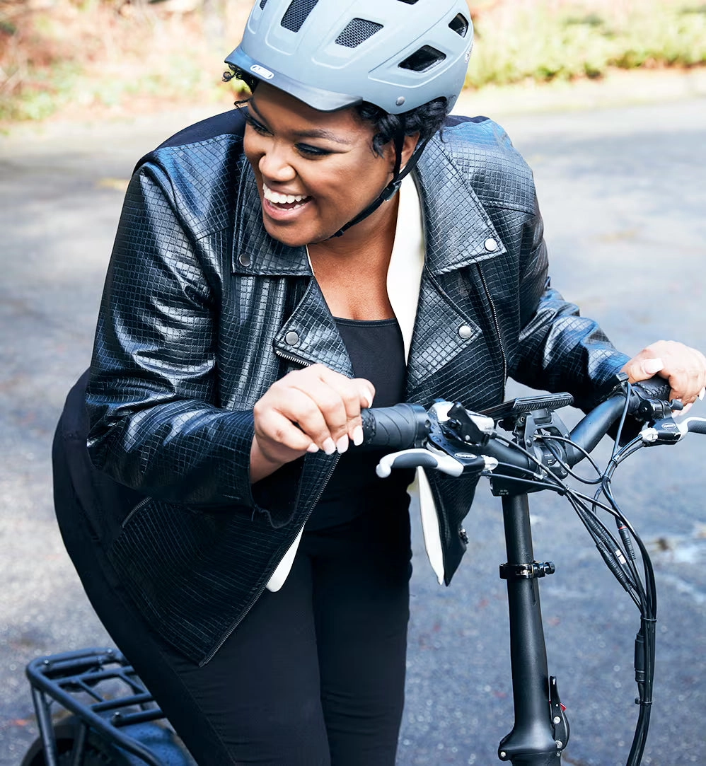 A smiling rider in a helmet and leather jacket walks a folding Rad ebike