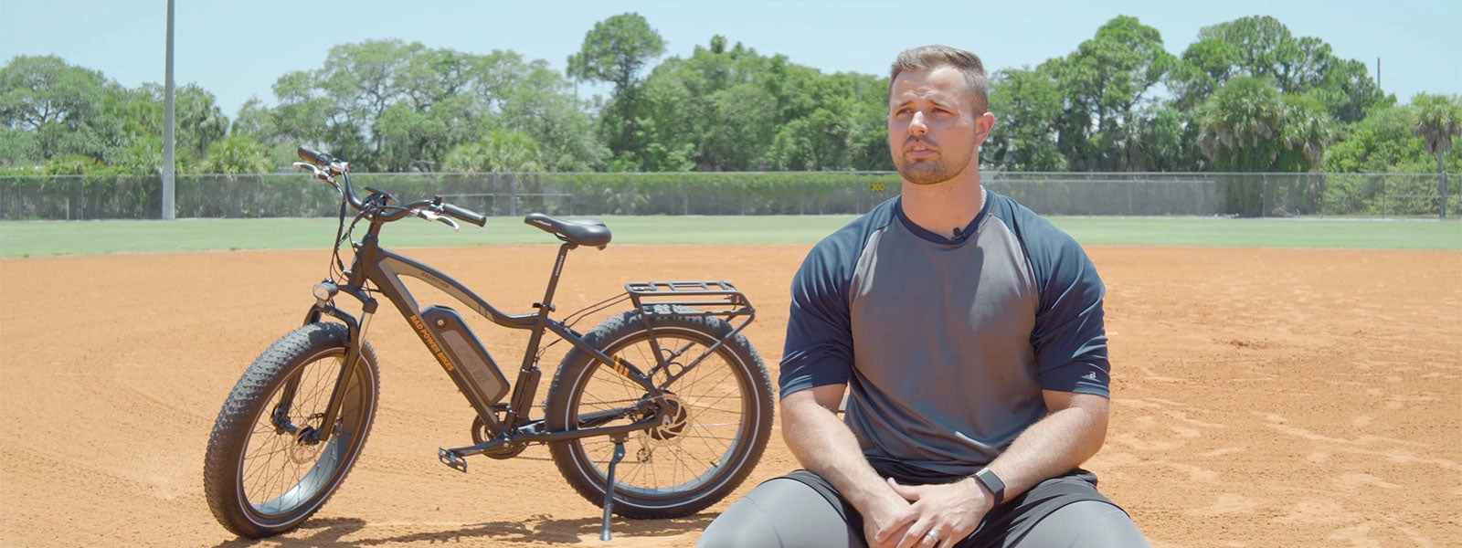 A baseball player sits on a dirt field beside a Rad ebike