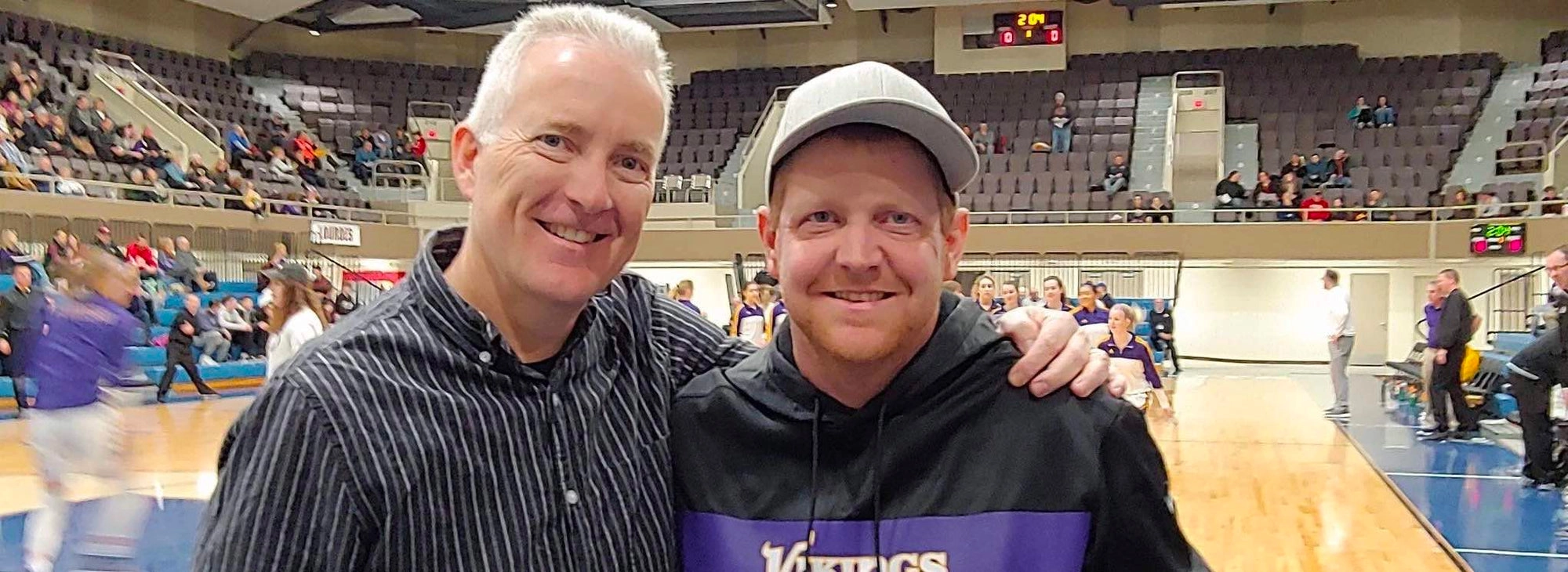Two smiling men pose together in an arena