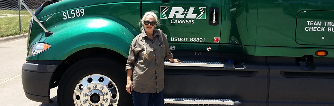 A woman stands beside a green semi-truck cab