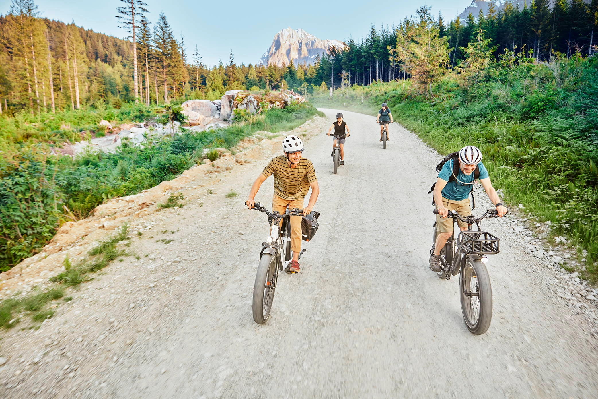 Three riders on ebikes roll down a gravel road toward distant mountains